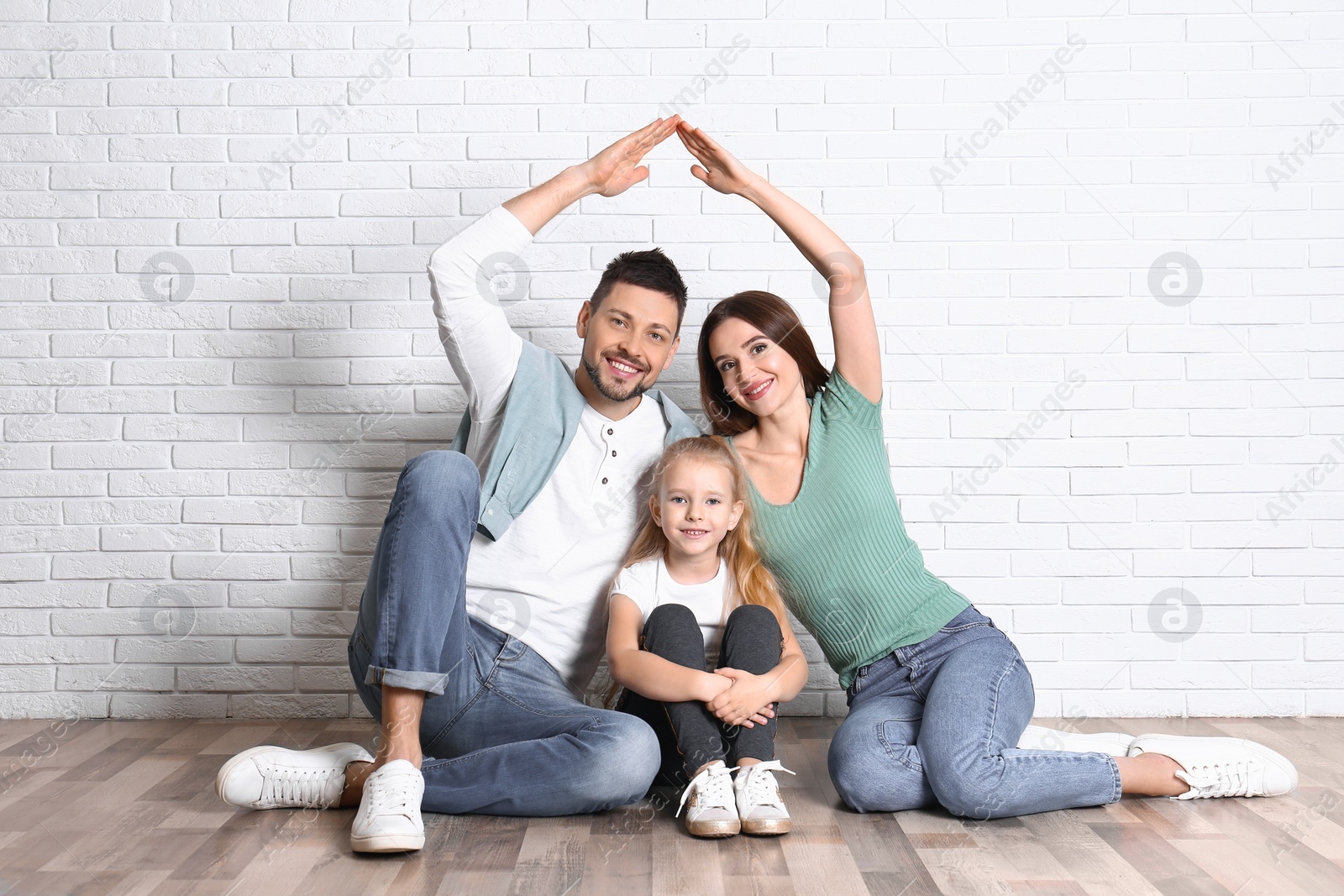 Photo of Happy family forming roof with their hands near brick wall. Insurance concept