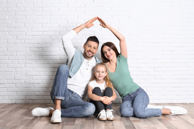 Happy family forming roof with their hands near brick wall. Insurance concept