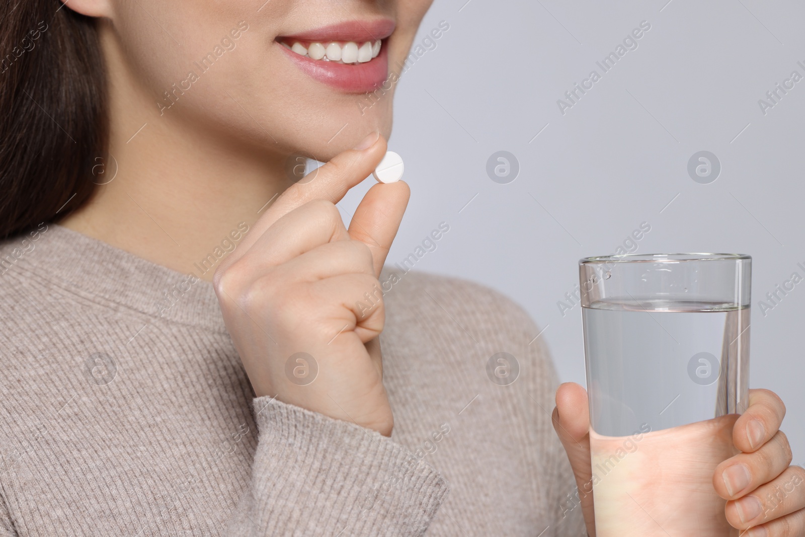 Photo of Woman with glass of water taking pill on gray background, closeup
