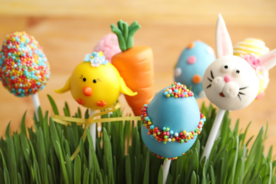 Photo of Delicious sweet cake pops in green grass, closeup. Easter holiday