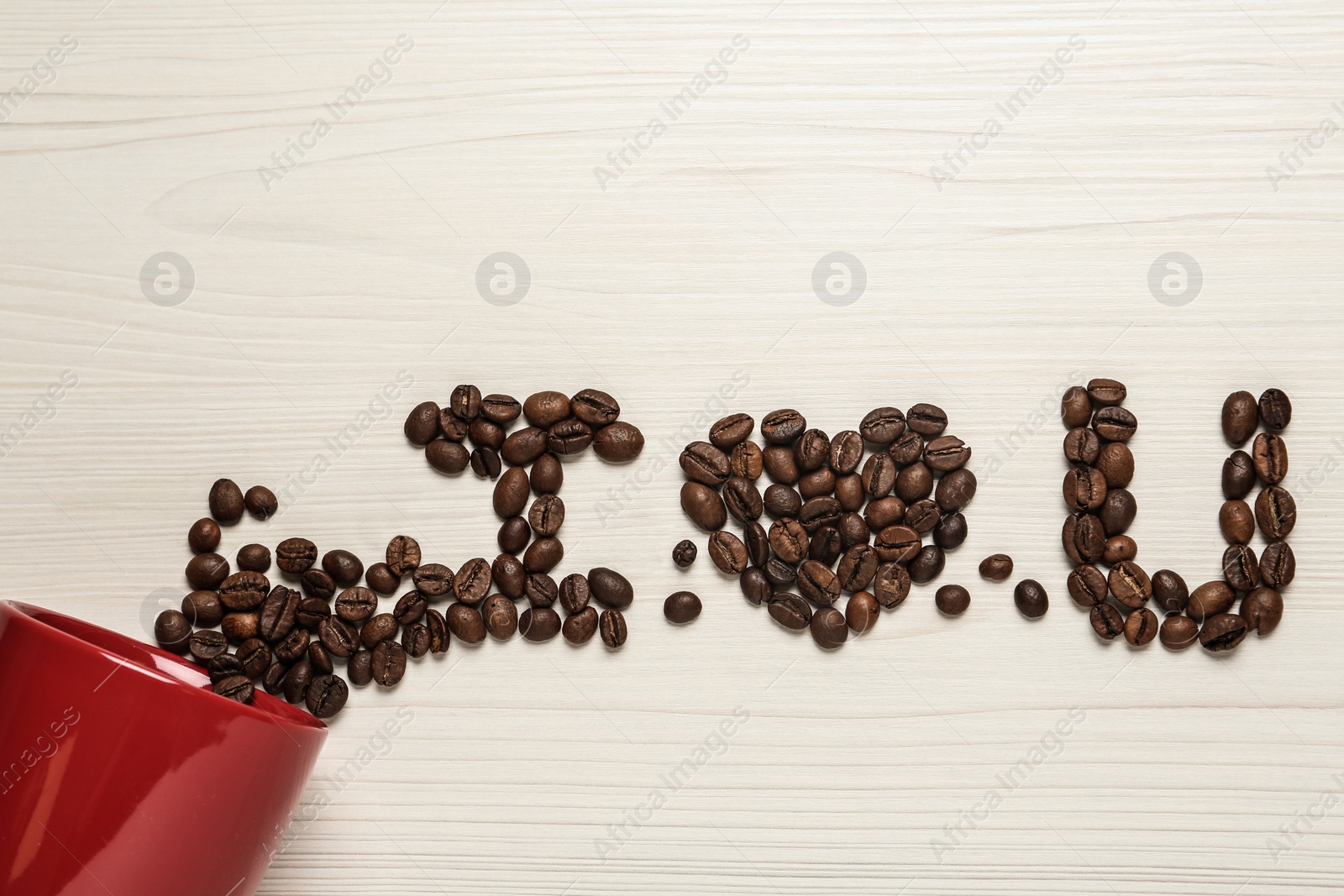 Photo of Phrase I Love You made of scattered coffee beans from red cup on white wooden table, flat lay