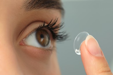 Photo of Woman putting contact lens in her eye on grey background, closeup