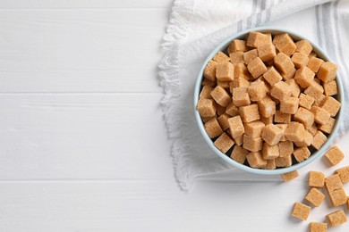 Photo of Bowl of brown sugar cubes on white wooden table, flat lay. Space for text