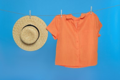 Photo of Hat and shirt drying on laundry line against light blue background