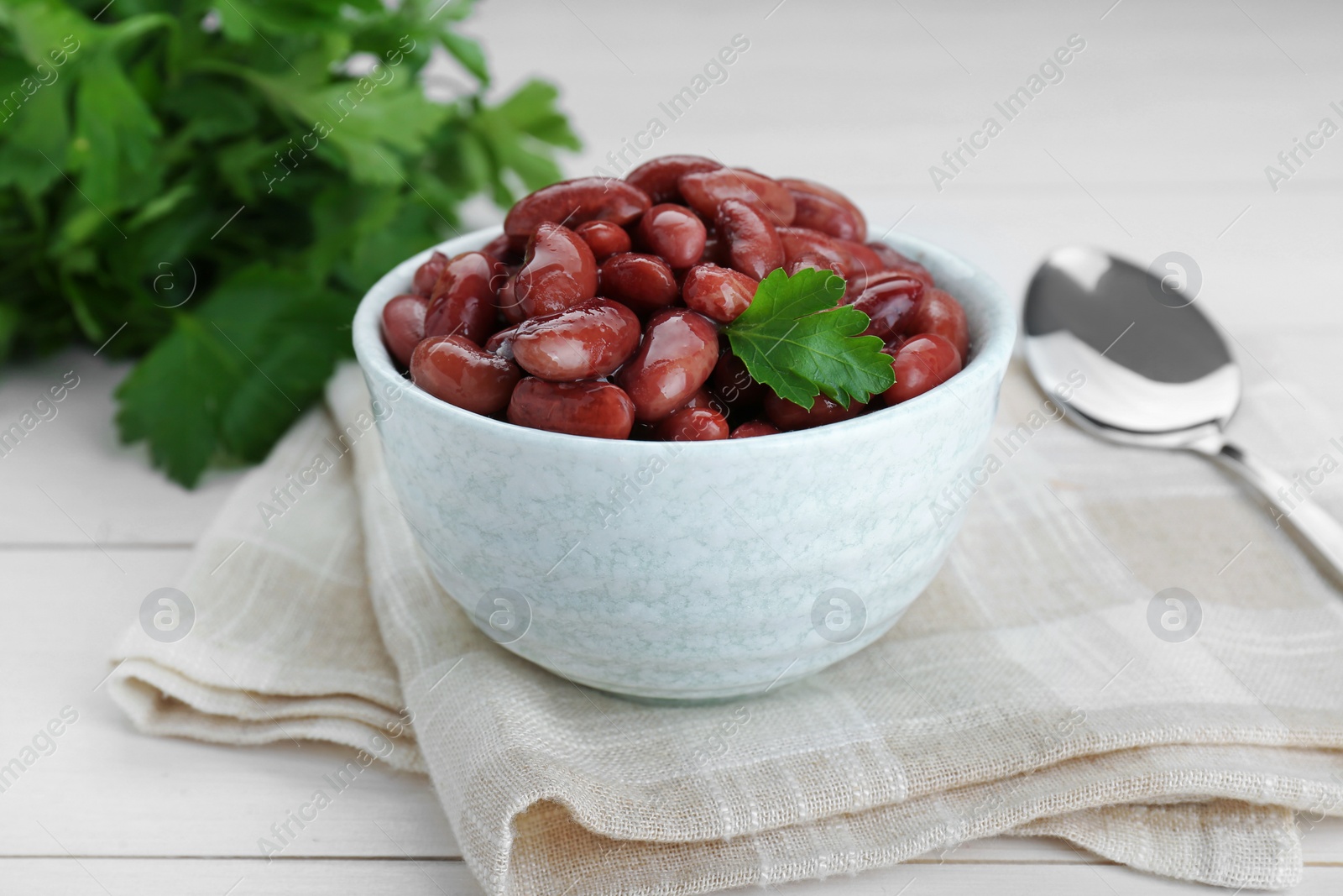 Photo of Bowl of canned kidney beans with parsley on white wooden table, closeup