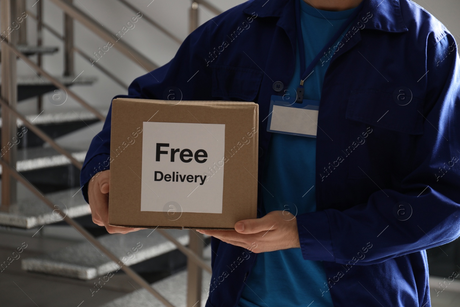 Photo of Courier holding parcel with sticker Free Delivery indoors, closeup