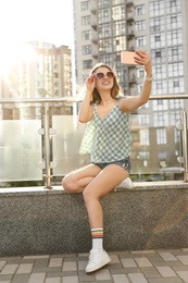 Photo of Beautiful young woman with sunglasses taking selfie outdoors