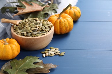 Bowl with seeds, fresh pumpkins and dry leaves on blue wooden table. Space for text