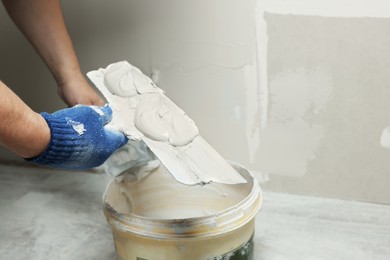 Photo of Professional worker holding putty knife with plaster indoors, closeup. Space for text