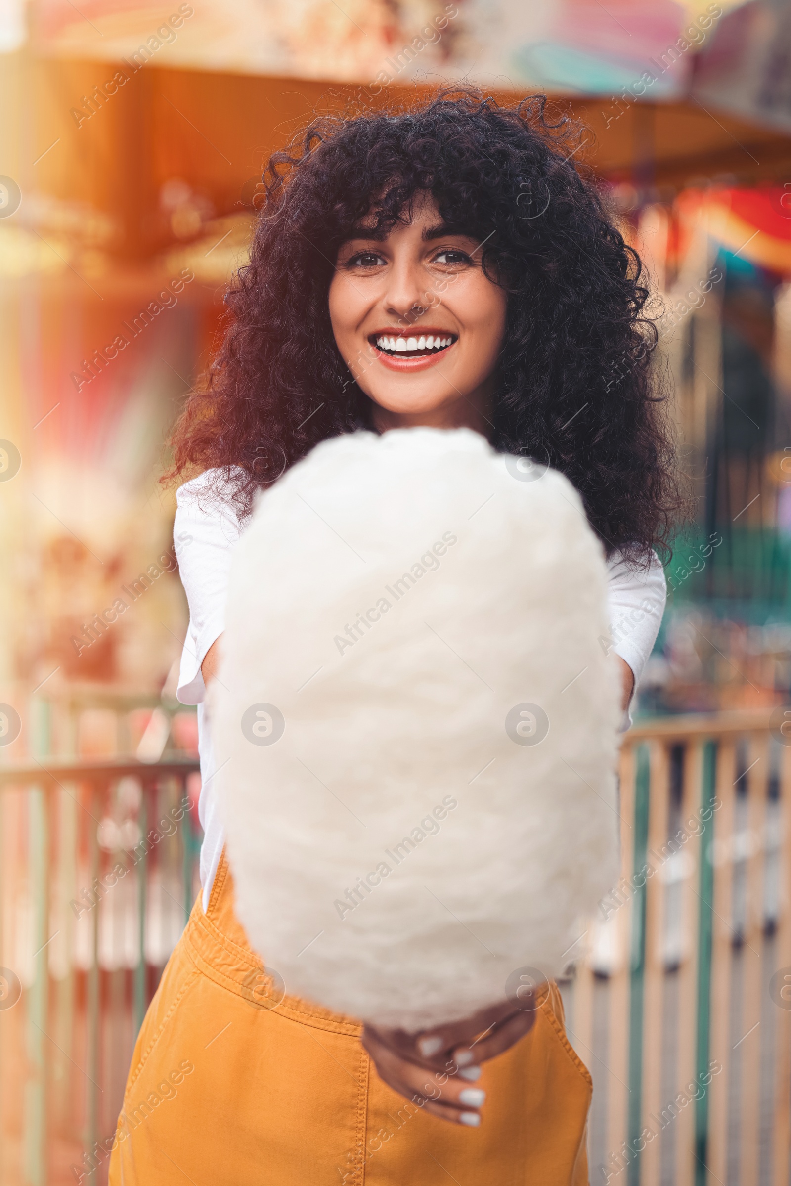 Image of Smiling woman with cotton candy at funfair on sunny day