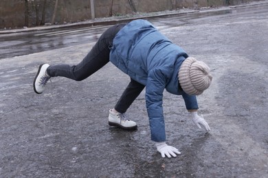 Photo of Young woman having difficulties with moving on icy road outdoors