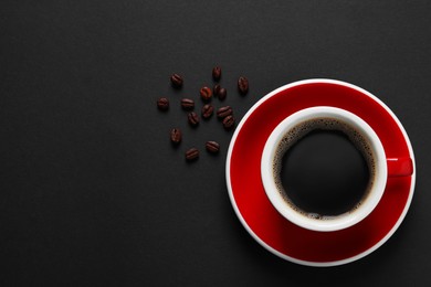 Cup with aromatic coffee and beans on black background, flat lay. Space for text