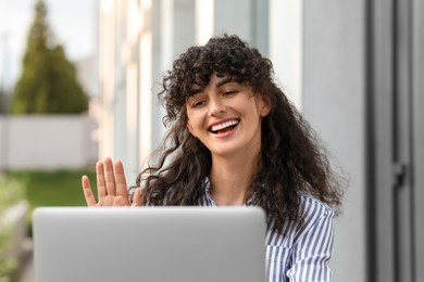 Happy young woman using modern laptop for video call outdoors