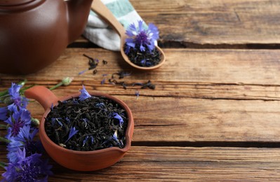 Photo of Dry tea leaves and cornflowers on wooden table. Space for text
