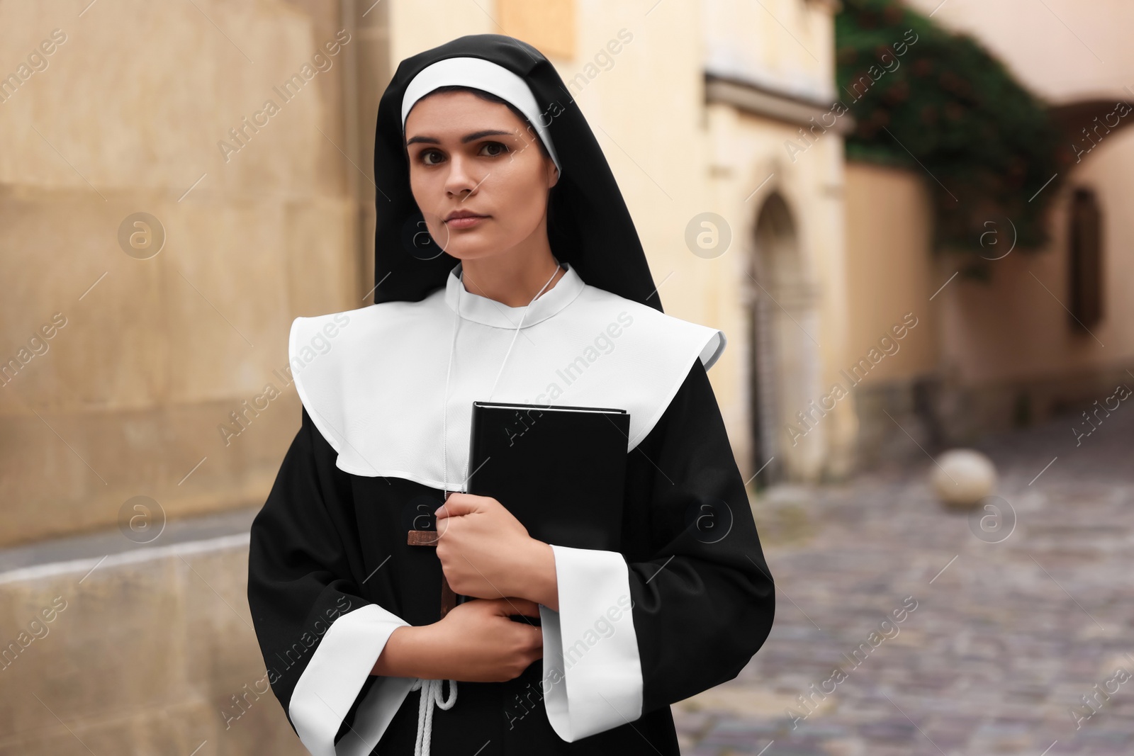 Photo of Young nun with Christian cross and Bible near building outdoors