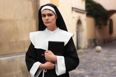 Photo of Young nun with Christian cross and Bible near building outdoors