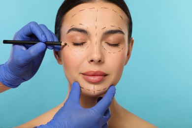 Photo of Doctor with pencil preparing patient for cosmetic surgery operation on light blue background, closeup