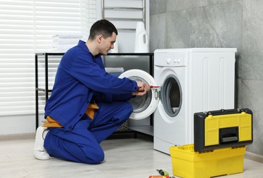 Young plumber repairing washing machine in bathroom