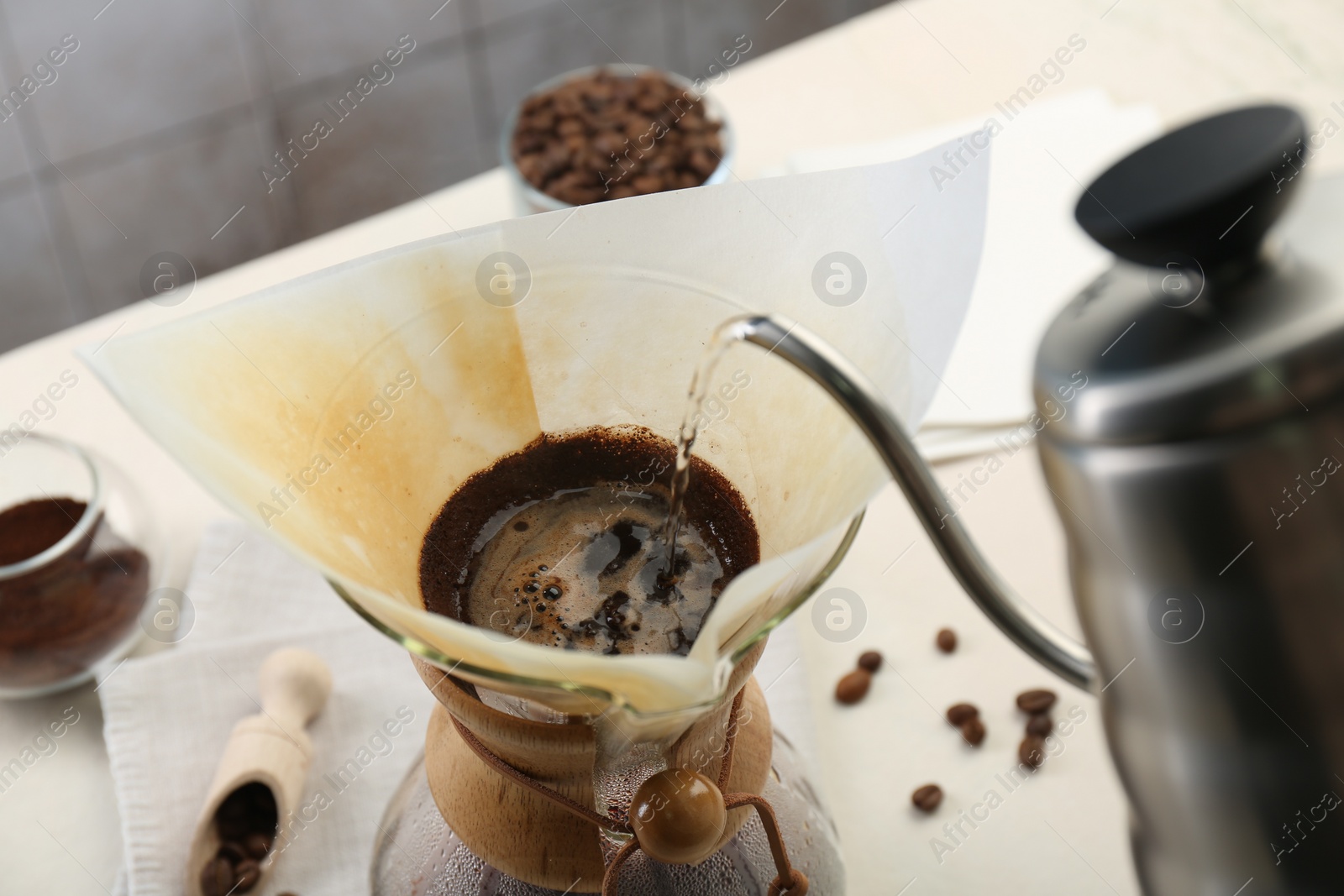 Photo of Making drip coffee. Pouring hot water into chemex coffeemaker with paper filter at table, closeup