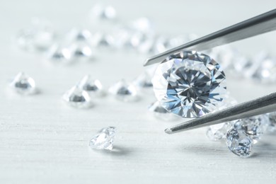 Tweezers with beautiful shiny diamond above light wooden table, closeup