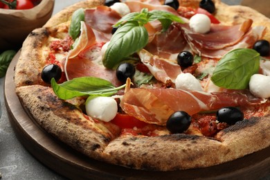 Photo of Tasty pizza with cured ham, olives, mozzarella cheese, sun-dried tomato and arugula on table, closeup