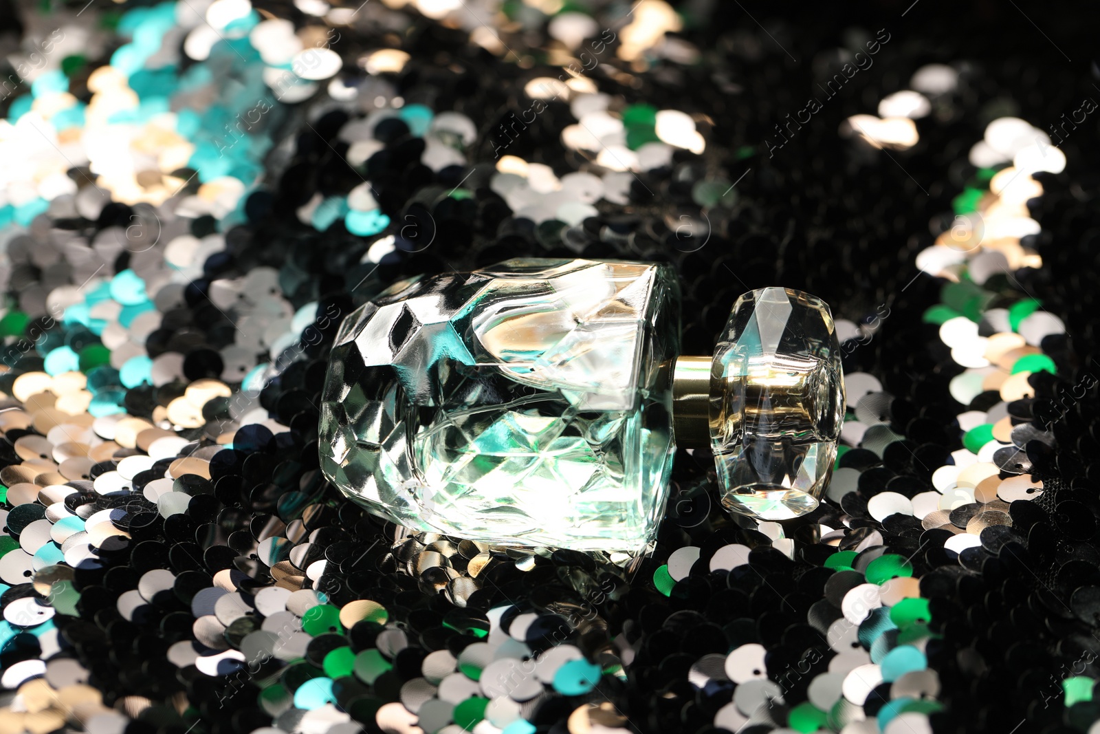 Photo of Luxury perfume in bottle on fabric with shiny sequins, closeup