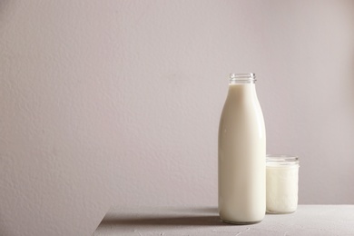 Photo of Bottle and glass with milk on table against grey wall