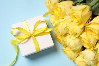 Beautiful bouquet of yellow roses and gift box on light blue background, flat lay