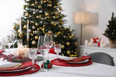 Photo of Christmas table setting with burning candles, gift box and dishware indoors