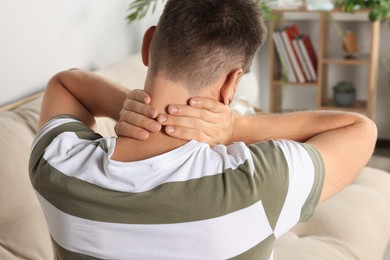 Photo of Man suffering from neck pain indoors, back view