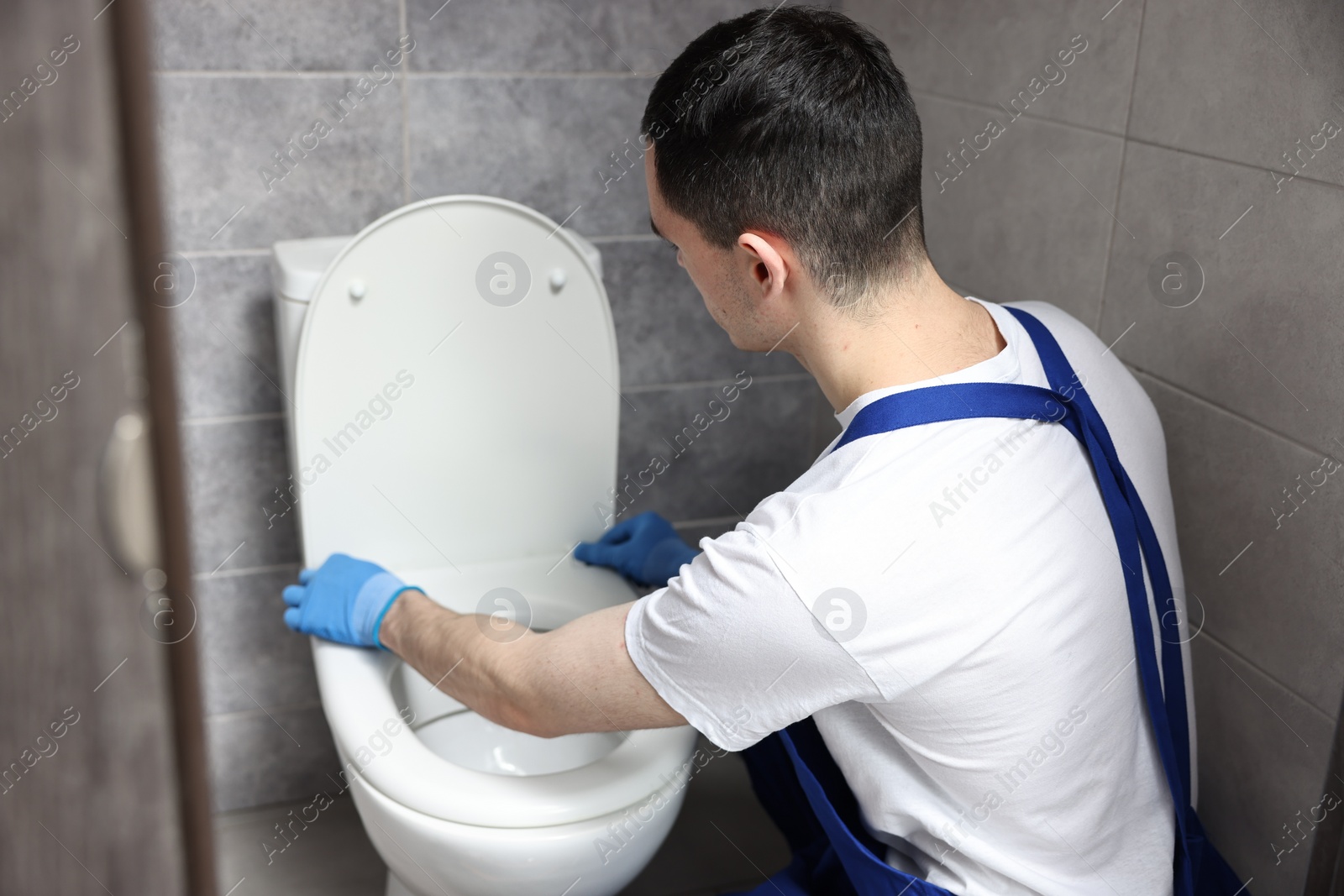 Photo of Young plumber wearing protective gloves repairing toilet bowl in water closet