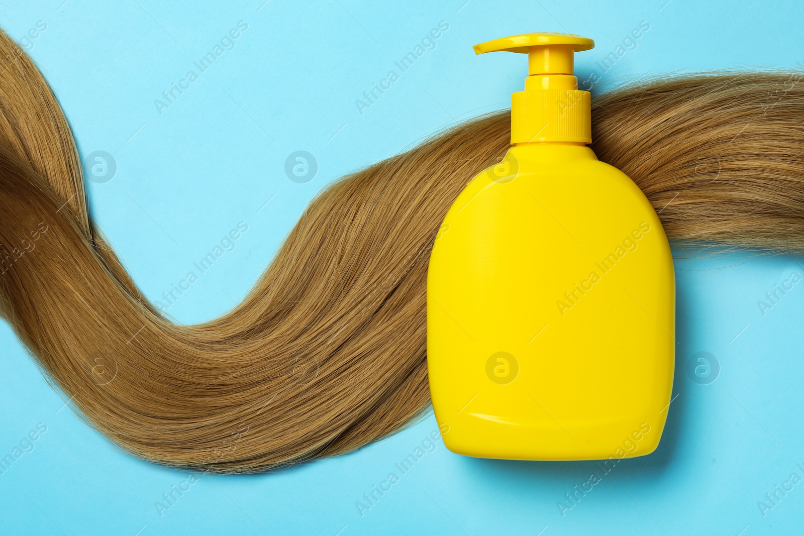 Photo of Blank bottle of cosmetic product and hair on light blue background, flat lay. Space for design