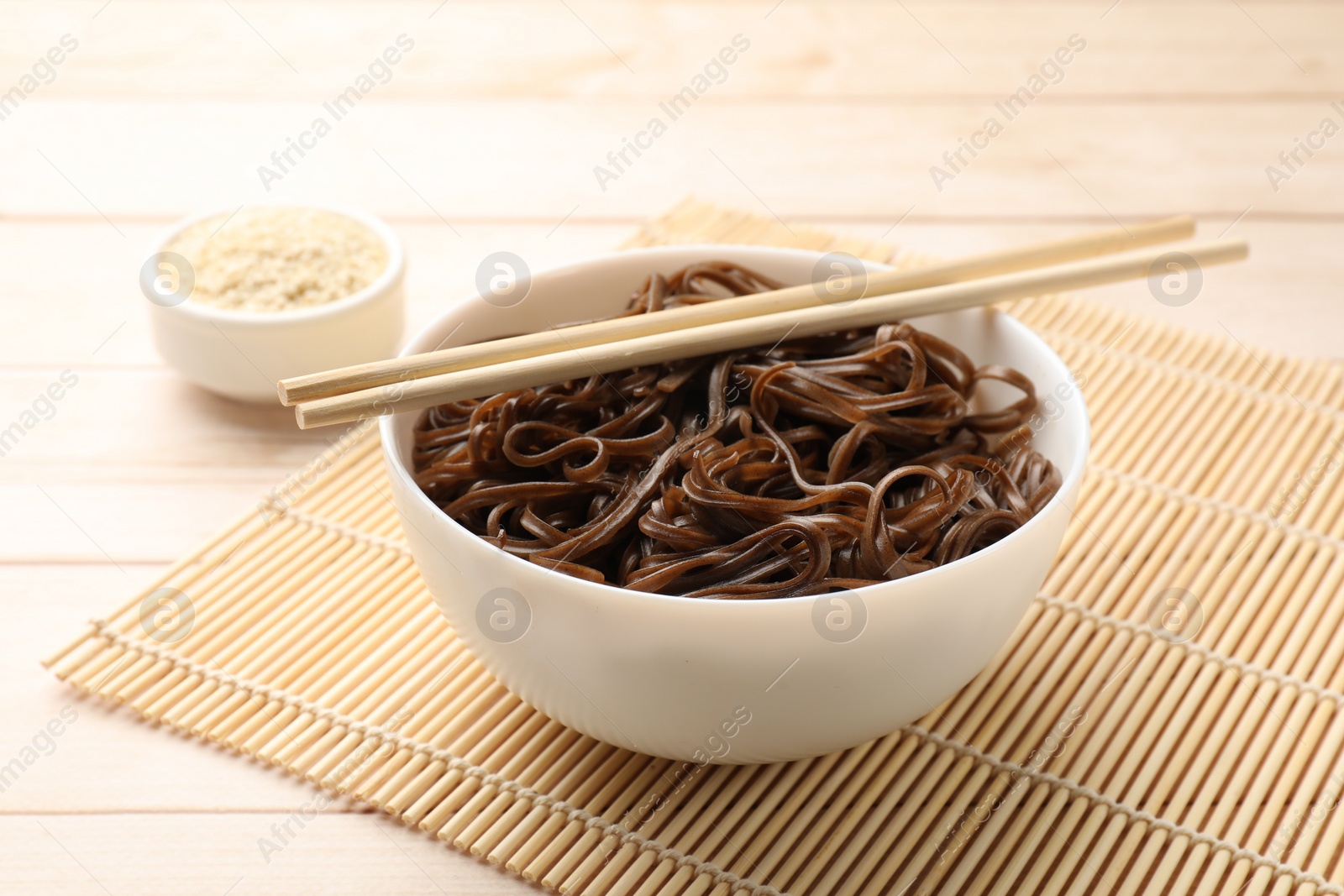 Photo of Tasty buckwheat noodles (soba) with sesame and chopsticks on wooden table