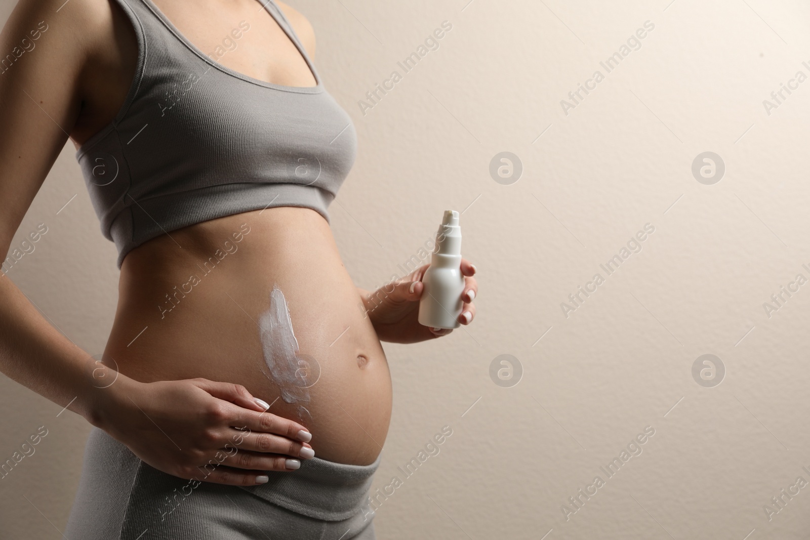 Photo of Pregnant woman applying cosmetic product on belly against beige background, closeup. Space for text