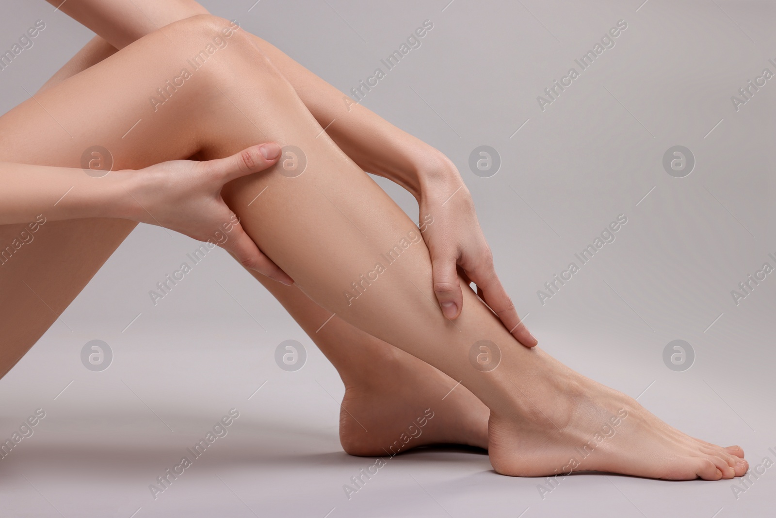 Photo of Woman suffering from leg pain on grey background, closeup