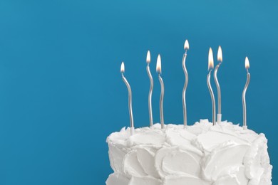 Photo of Delicious cake with cream and burning candles on light blue background, closeup. Space for text