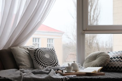 Photo of Comfortable lounge area with blanket and soft pillows near window in room