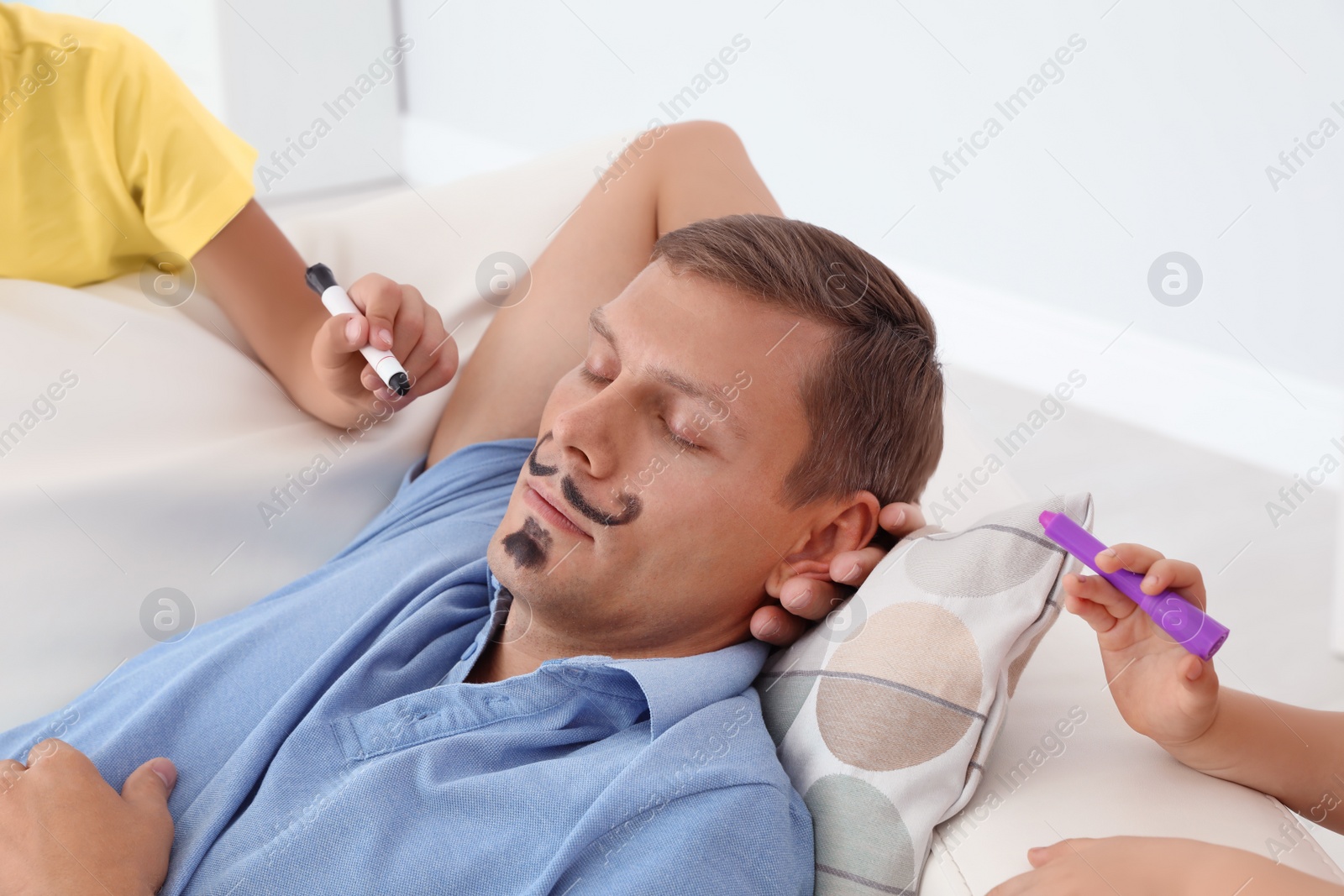 Photo of Little children painting their father's face while he sleeping on couch at home. April fool's day prank