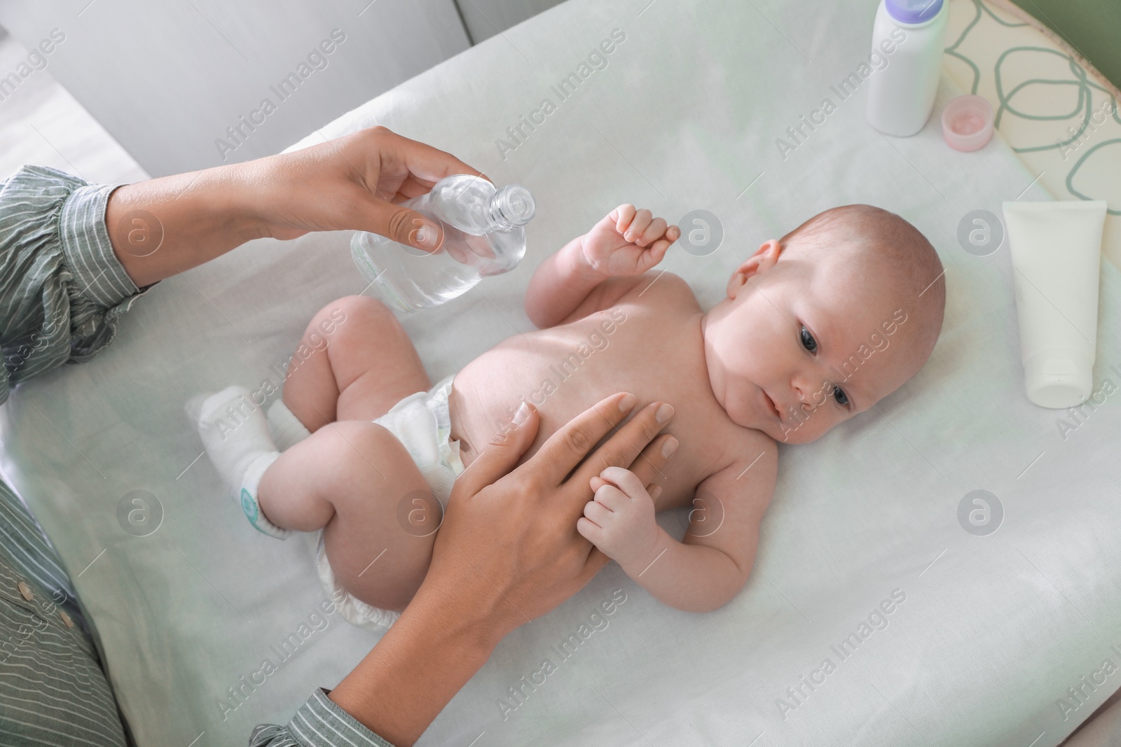 Photo of Mother massaging her baby with oil on changing table indoors, above view