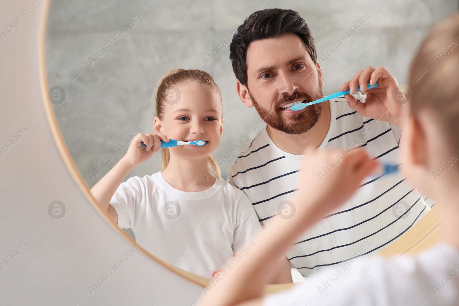 Photo of Father and his daughter brushing teeth together near mirror in bathroom