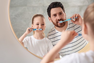 Father and his daughter brushing teeth together near mirror in bathroom