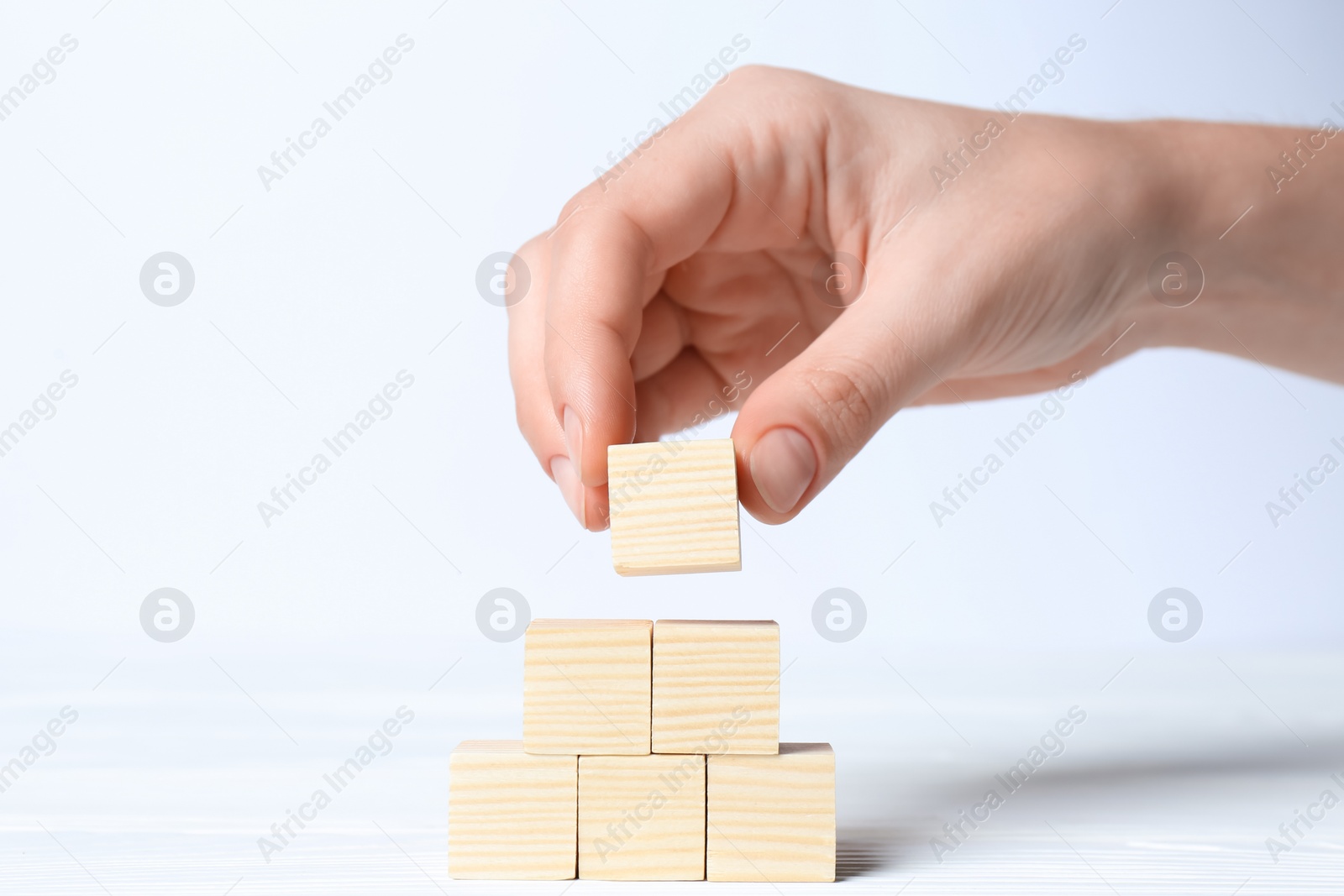 Photo of Woman building pyramid of cubes on white background, closeup with space for text. Idea concept