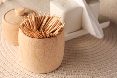 Photo of Wooden holder with many toothpicks on wicker mat, closeup. Space for text