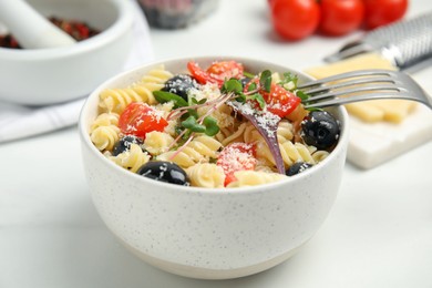Photo of Bowl of delicious pasta with tomatoes, olives and cheese on white table, closeup