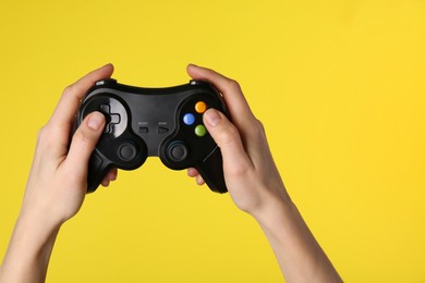 Woman using game controller on yellow background, closeup. Space for text