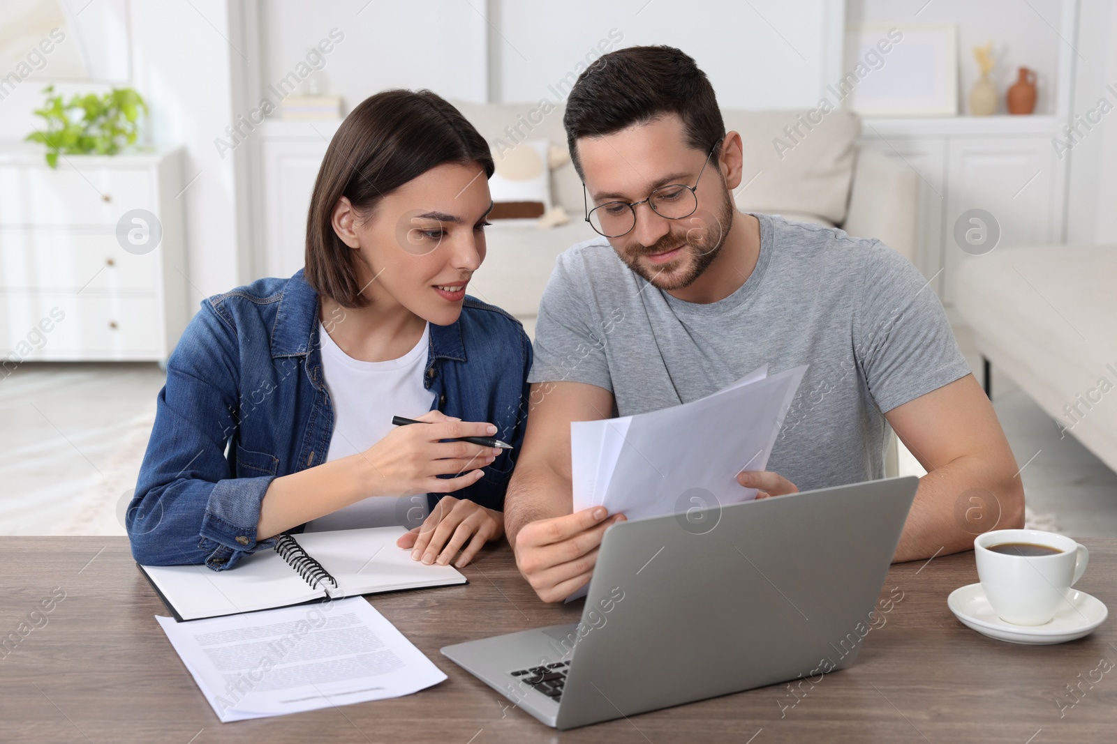 Photo of Young couple with papers discussing pension plan at wooden table indoors