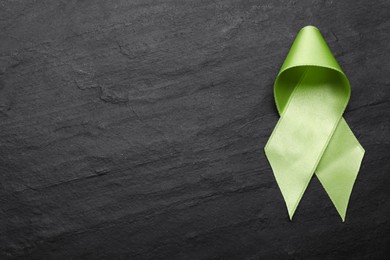 Photo of World Mental Health Day. Green ribbon on black background, top view with space for text