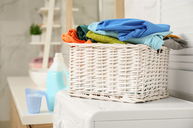 Photo of Wicker basket with laundry on washing machine in bathroom