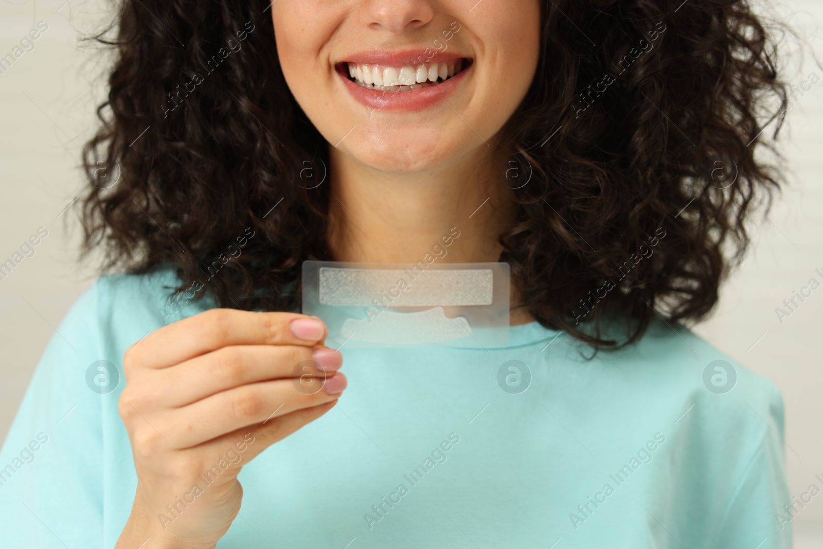 Photo of Young woman holding teeth whitening strips on light background, closeup