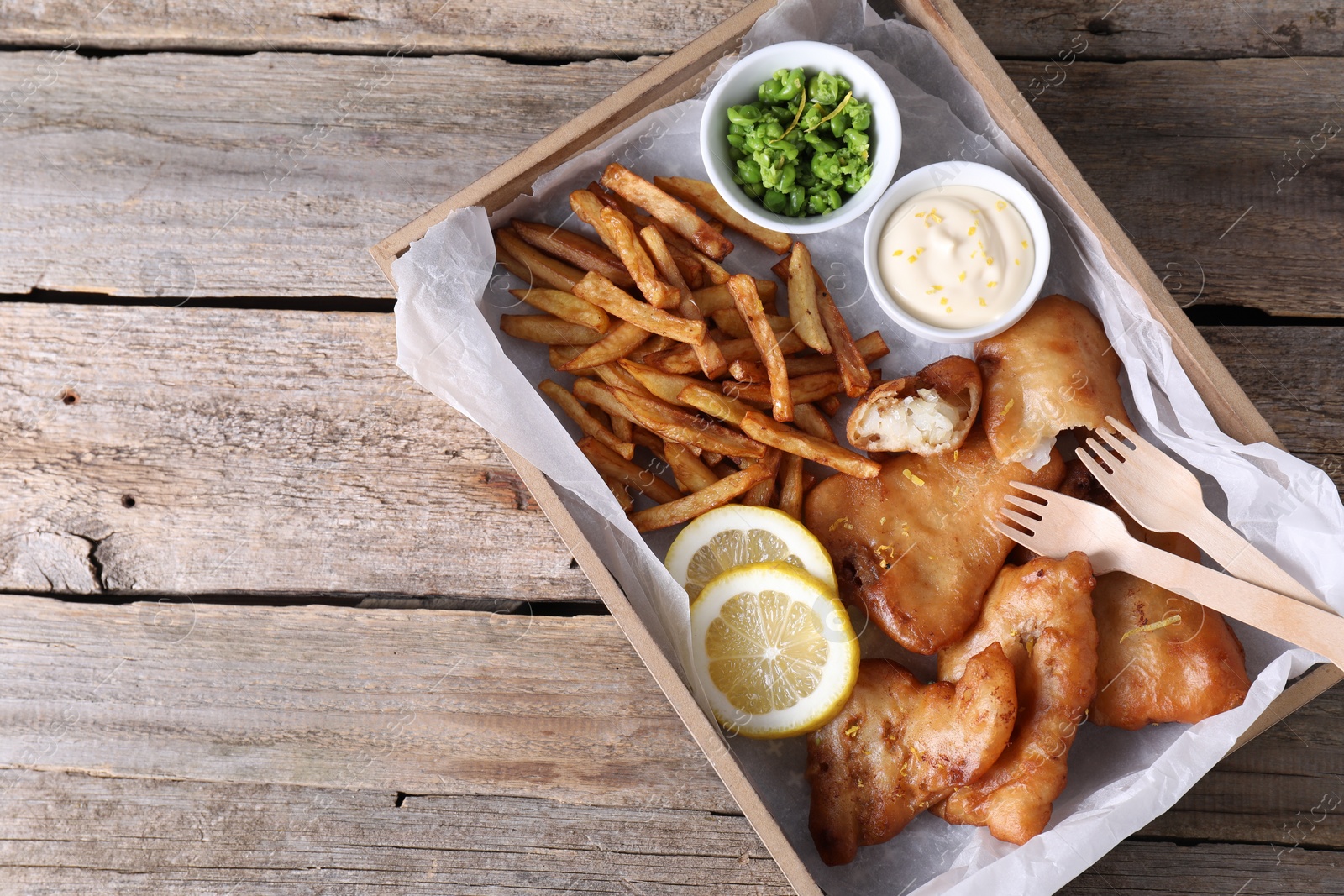 Photo of Tasty fish, chips, sauce and peas on wooden table, top view. Space for text